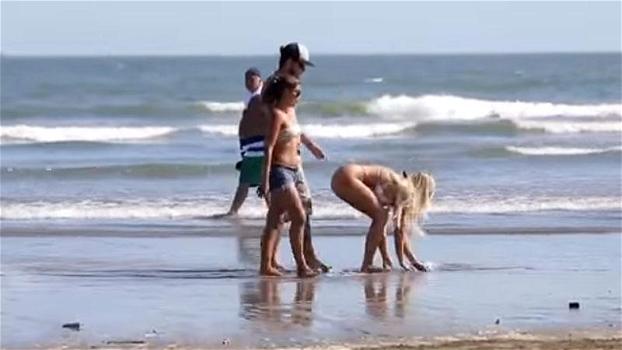 Una ragazza in bikini si piega davanti ai ragazzi in spiaggia. Ecco le reazioni delle fidanzate
