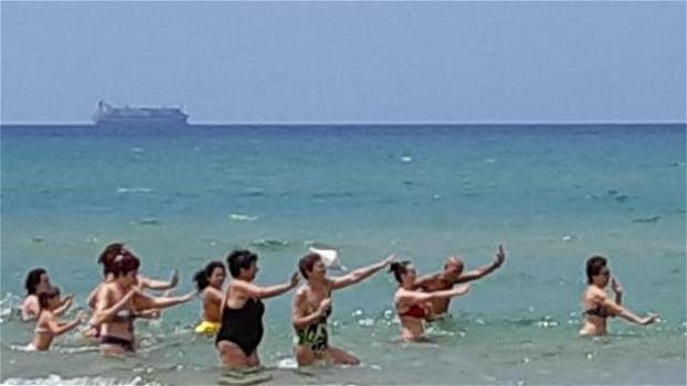 Balli di gruppo sulla spiaggia di Pozzallo: come sfondo il cargo carico di migranti