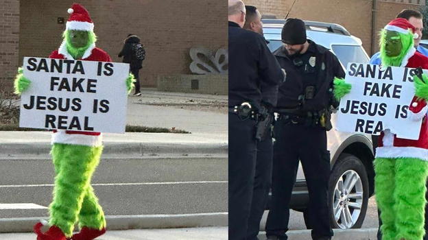 Vestito da Grinch davanti ad una elementare sfoggia un cartello: "Babbo Natale è finto, Gesù è reale"