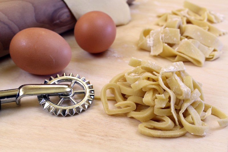 Preparazione della pasta fresca fatta in casa: Vista ravvicinata della mano  della donna che si tira un po' di fettuccine fresca sul tavolo da lavoro in  legno alla luce naturale del sole